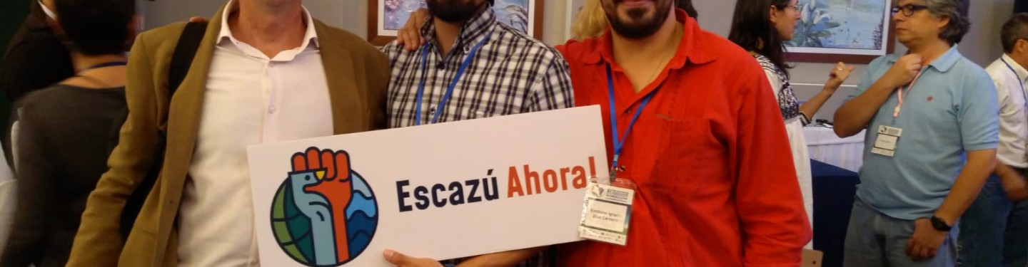 3 men standing together holding a sign that says Escazu