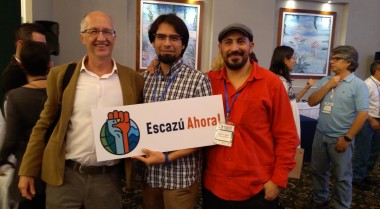 3 men standing together holding a sign that says Escazu